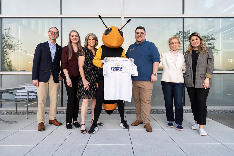 QEP facilitators pose with Georgia Tech's mascot, Buzz, holding a T-shirt with the Leaders in Progress and Service graphic on it.