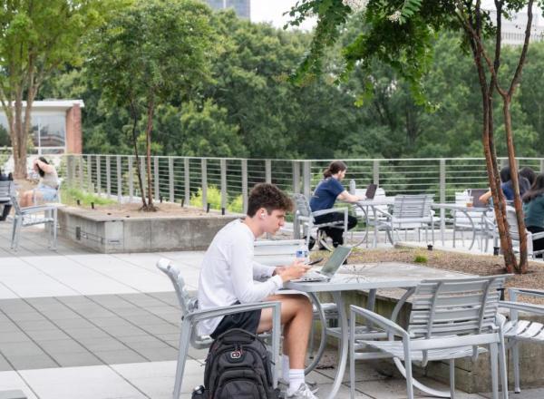 Students study and relax on a rooftop terrace surrounded by trees and modern outdoor seating.